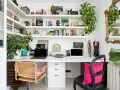 Un despacho en casa con estanterías llenas de libros y plantas. Dos portátiles, una impresora y decoración variada crean un espacio de trabajo funcional y acogedor.