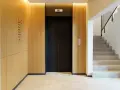 Portal moderno con ascensor negro y escaleras de mármol. Ideas para como decorar un portal de vecinos con paneles de madera y luz cálida.