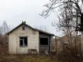 Casa de ladrillo blanco, abandonada, con ventanas rotas y vegetación seca. Un ejemplo de la ley sobre casas abandonadas.