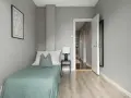 Habitación minimalista con cama individual, mesita de noche y lámpara. La puerta abierta revela un pasillo, sugiriendo que es legal alquilar habitaciones.