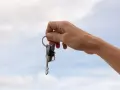 Mano sostiene un llavero con dos llaves y un dije de casa. La custodia llaves comunidad representa el acceso a un hogar compartido.