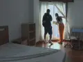 Pareja joven revisando un apartamento con cama, estantería y escritorio.