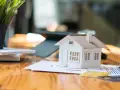 Maqueta de casa sobre gráficos, sugiriendo cómo saber si una casa tiene cargas. Llaves y tarjetas de crédito cerca.