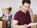 Hombre habla por teléfono, revisando papeles, mientras una mujer desempaca. Quizás buscando como saber a quien pertenece un terreno.