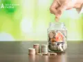 Mano deposita moneda en alcancía con casa, pensando qué pasa si no pago el último mes de alquiler.