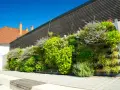 Un exuberante jardín vertical con palets y macetas, lleno de plantas verdes y flores moradas, adorna una pared de madera oscura.