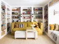 Sofá amarillo y estanterías llenas de libros, como si fueran casas que no necesitan permiso de obra. Un espacio acogedor para leer.