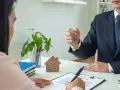 Agente inmobiliario entrega llaves a cliente. Un modelo de casa y un contrato sobre la mesa, ideal para referencia precios alquiler.
