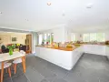 Cocina moderna con suelo gris y muebles blancos. Una mesa con sillas de madera y un jarrón con flores completan la escena.