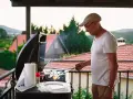 Hombre mayor cocina en barbacoa en terraza. ¡Cuidado con las multas por hacer barbacoas en terrazas!