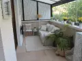 Acogedor salón en terrazas cerradas con encanto, con sofá, silla, plantas y vistas al exterior.