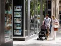 Pareja pasea con carrito, mirando escaparate inmobiliario. Quizás planean donar un piso a un hijo en Cataluña.
