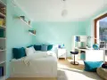 Habitación con pared verde menta y gris, cama blanca, estanterías y escritorio.