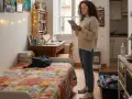 Joven revisa en su tablet qué necesito para empadronarme en un piso de alquiler. Habitación con cama, escritorio y estanterías.