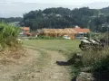 Terreno rural con construcción de madera, casas y vegetación. Se observa un camino de tierra y una posible servidumbre de acueducto en el paisaje.