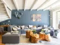 Sofá modular gris y pared azul crean un ambiente acogedor. Mesas de tronco y detalles en madera aportan calidez.