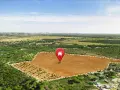 Vista aérea de varios tipos de terrenos: un campo marrón arado, un bosque de pinos y un área residencial.