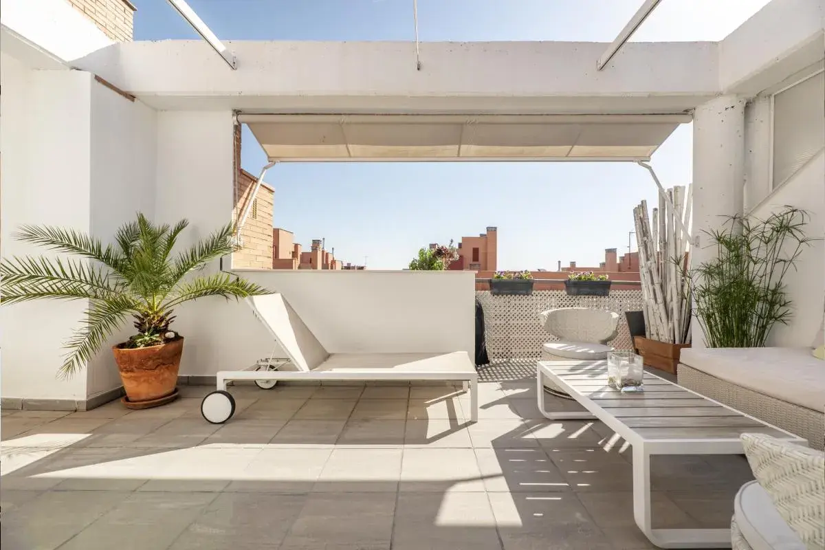 Encantadora decoracion terrazas aticos: tumbona, mesa de centro, sillón y plantas crean un oasis urbano.