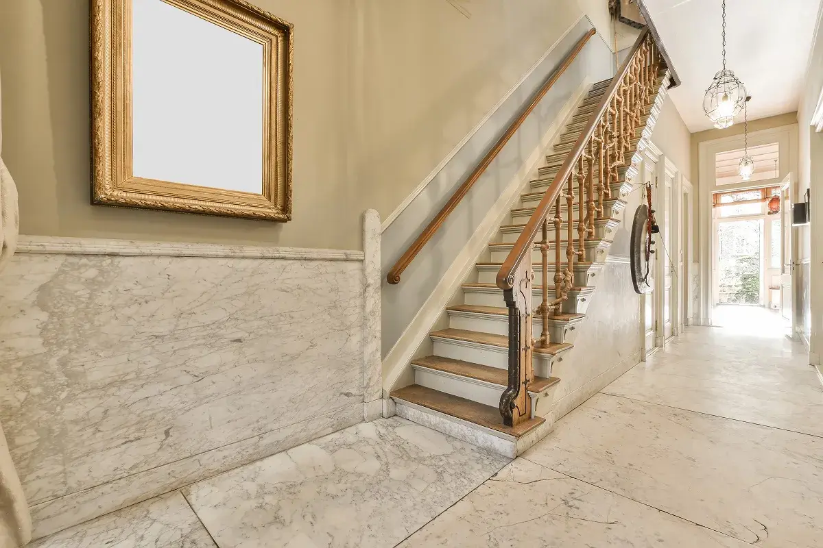 Elegante escalera con barandilla de madera y mármol para decorar rellano escalera comunidad. Un cuadro dorado adorna la pared.