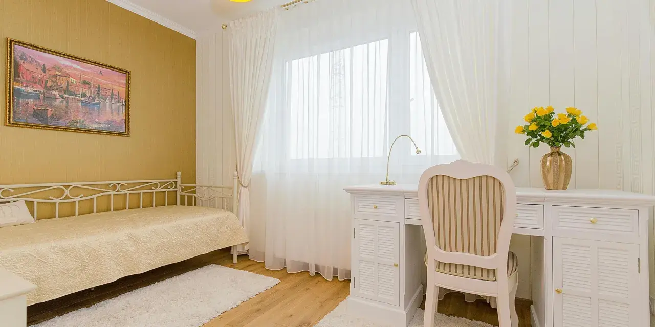 Dormitorio con paredes doradas, cama blanca y escritorio. Los colores que combinan con el amarillo en paredes son el blanco y los tonos tierra, creando un ambiente cálido y luminoso.