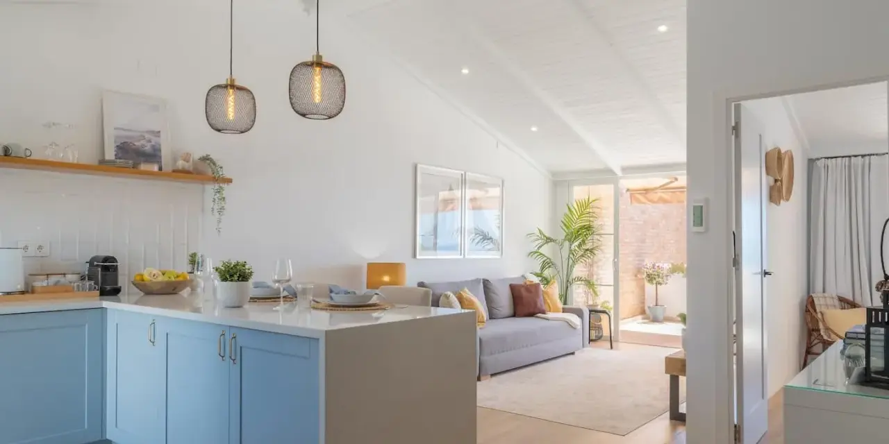 Cocina y sala de estar luminosas, perfectas para decorar casa playa poco presupuesto. Muebles claros, plantas y detalles náuticos crean un ambiente fresco.