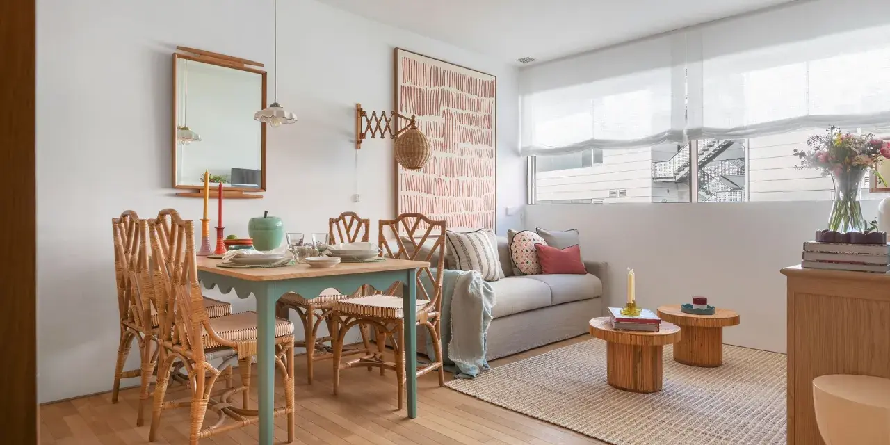 Ideas para decorar un piso pequeño con poco dinero: mesa de comedor de ratán, sofá acogedor y arte de pared llamativo.