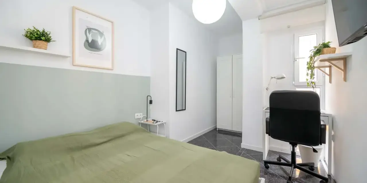 Habitación luminosa con cama, escritorio y armario. Ideal como piso para estudiantes, con decoración moderna y plantas.