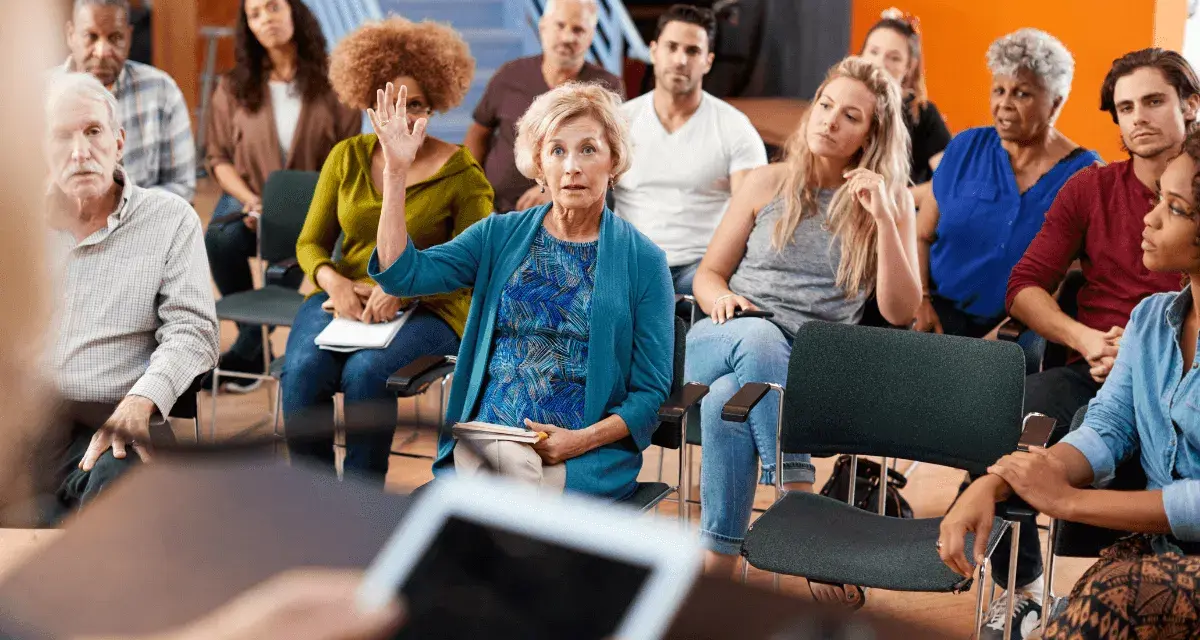Una mujer levanta la mano en una reunión, mostrando que cualquiera puede ser presidente de una comunidad.