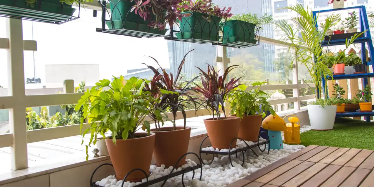 Balcón lleno de plantas en macetas, ideal para decorar terrazas barato. Césped artificial y suelo de madera completan el espacio.
