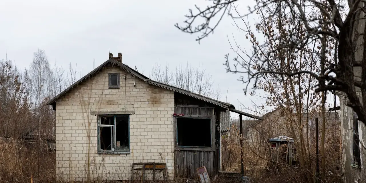 Casa de ladrillo blanco, abandonada, con ventanas rotas y vegetación seca. Un ejemplo de la ley sobre casas abandonadas.