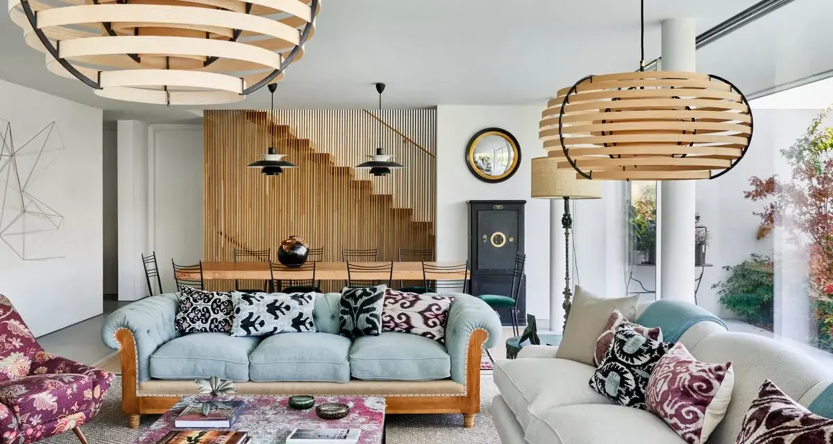 Elegante salón con sofás claros, mesa de centro con libros y lámparas de madera. El minimalismo en casa se refleja en la escalera de madera y la decoración cuidada.