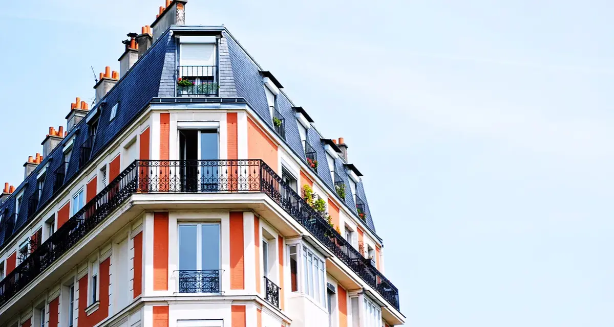 Edificio parisino con tejado mansarda y balcones de hierro forjado. Las fachadas naranjas y blancas, con chimeneas, parecen fuera de ordenación por su diseño único.