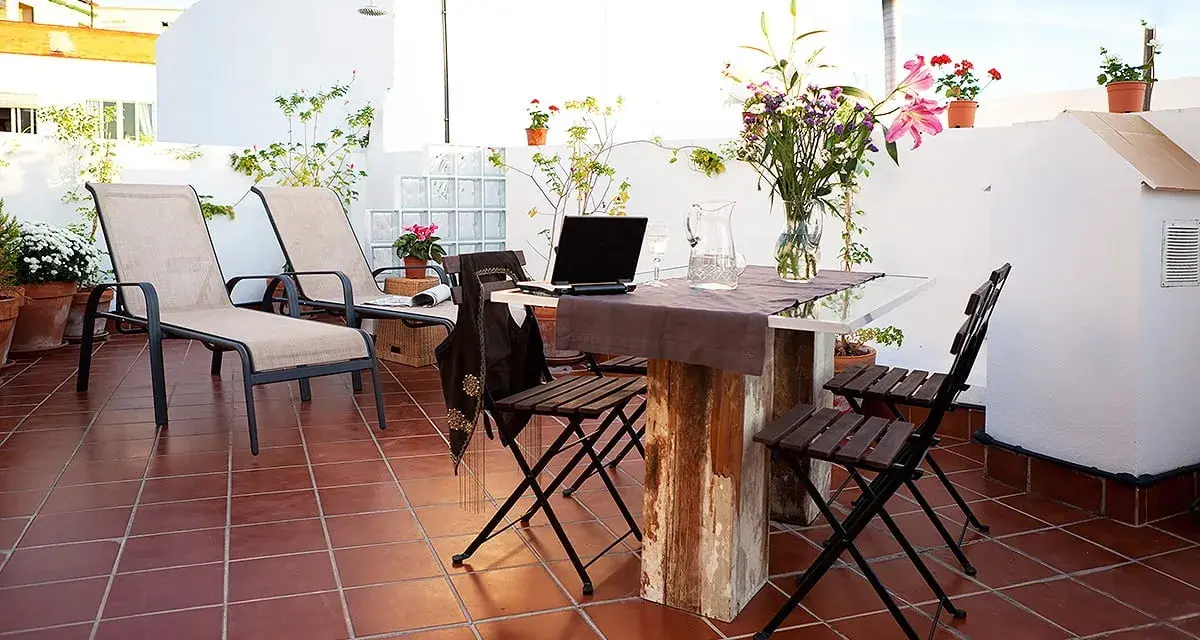 Terraza con tumbonas, mesa y sillas, ideal para uso privativo. Flores y plantas decoran el espacio.