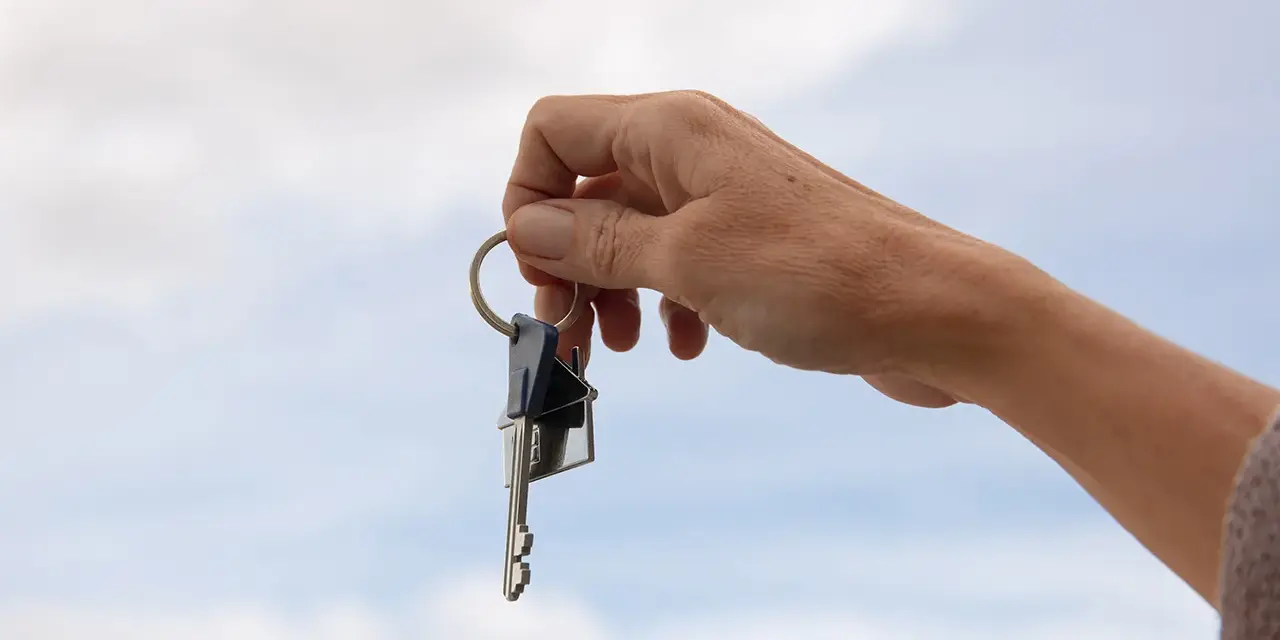 Mano sostiene un llavero con dos llaves y un dije de casa. La custodia llaves comunidad representa el acceso a un hogar compartido.