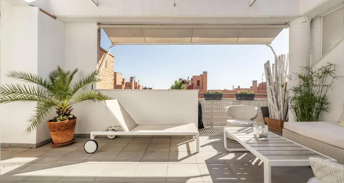 Encantadora decoracion terrazas aticos: tumbona, mesa de centro, sillón y plantas crean un oasis urbano.