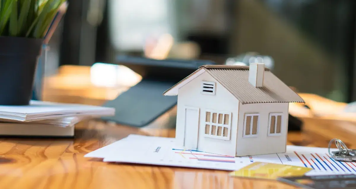 Maqueta de casa sobre gráficos, sugiriendo cómo saber si una casa tiene cargas. Llaves y tarjetas de crédito cerca.