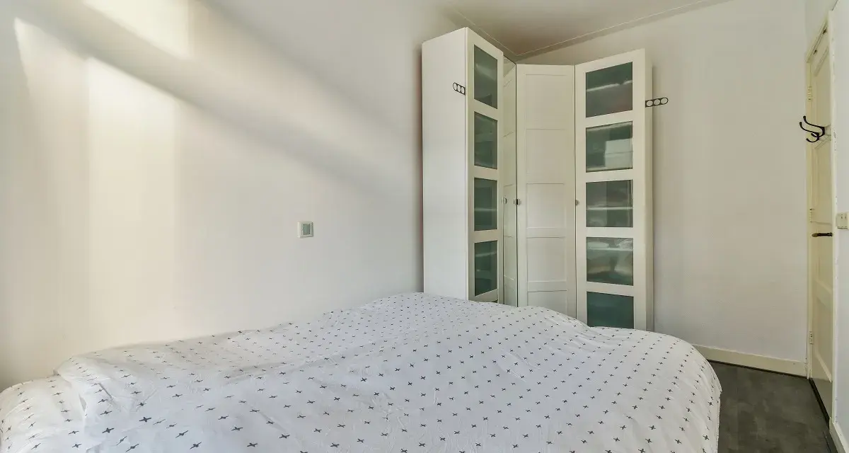 Un armario blanco con puertas de cristal es una solución ideal para saber donde colocar el armario en un dormitorio pequeño, maximizando el espacio.
