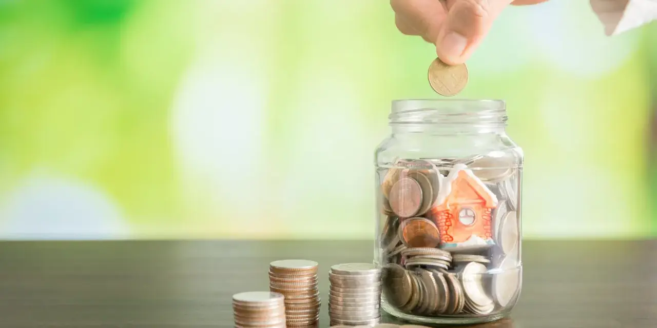 Mano deposita moneda en alcancía con casa, pensando qué pasa si no pago el último mes de alquiler.