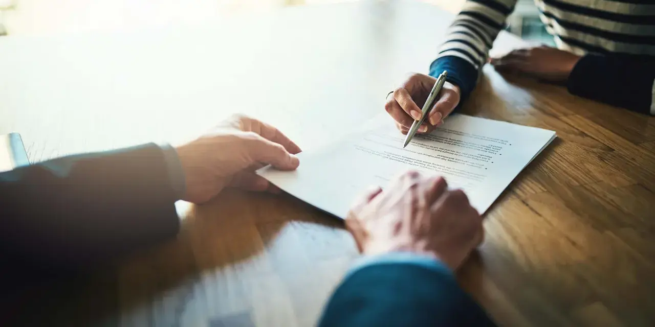 Manos firmando un contrato de alquiler de piso. Los padres avalan el alquiler.