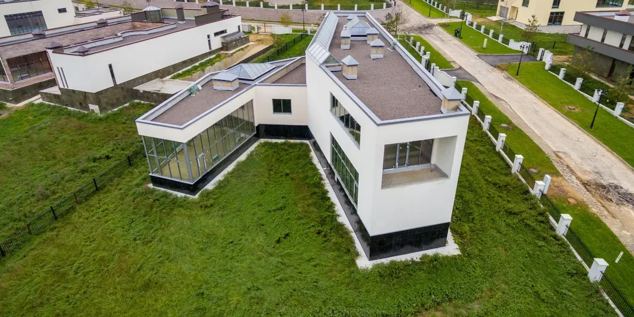 Casa moderna con grandes ventanales y tejado plano, rodeada de césped. Se puede poner una casa prefabricada en un terreno urbano como esta.