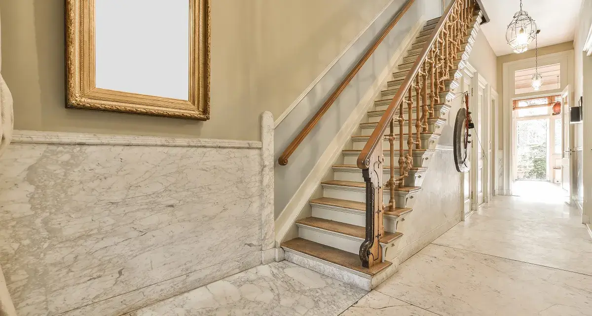 Elegante escalera con barandilla de madera y mármol para decorar rellano escalera comunidad. Un cuadro dorado adorna la pared.