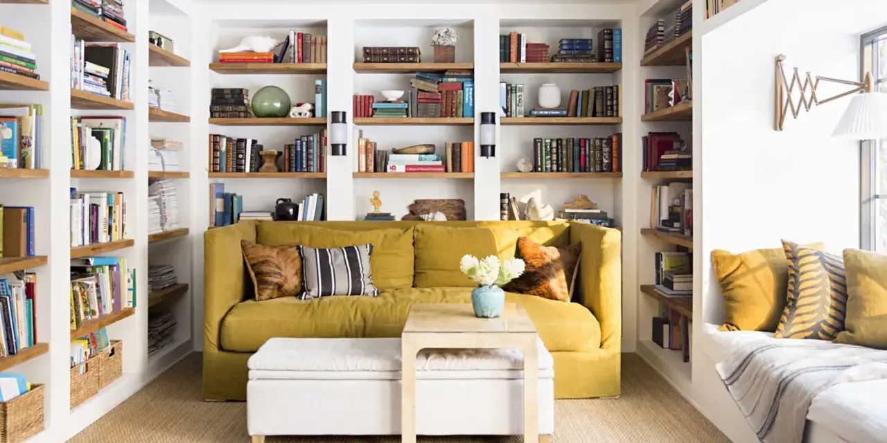 Sofá amarillo y estanterías llenas de libros, como si fueran casas que no necesitan permiso de obra. Un espacio acogedor para leer.