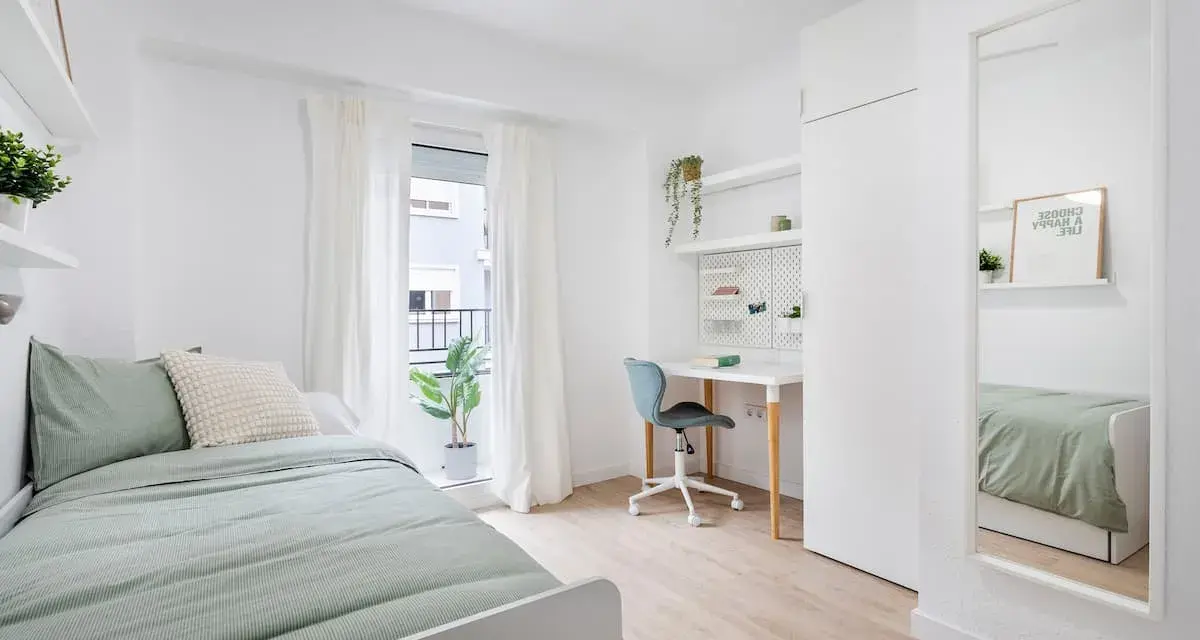 Habitación de estudiante con cama, escritorio, silla y espejo.