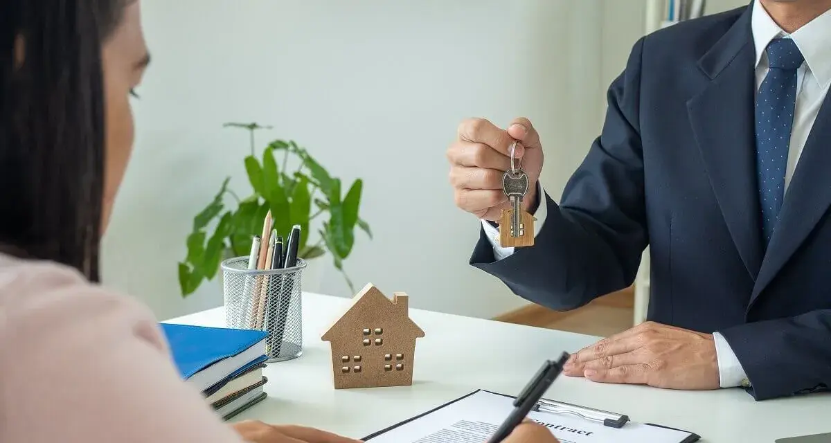 Agente inmobiliario entrega llaves a cliente. Un modelo de casa y un contrato sobre la mesa, ideal para referencia precios alquiler.