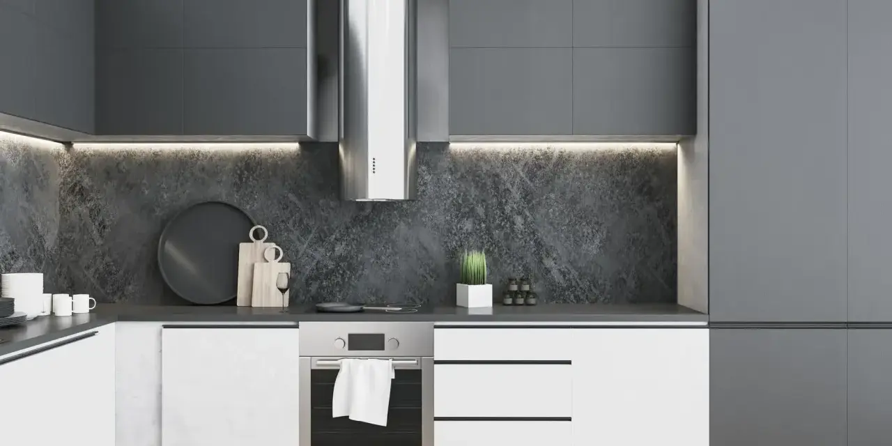 Moderna cocina blanca y gris oscuro con campana extractora de acero inoxidable, encimera de piedra y armarios minimalistas.