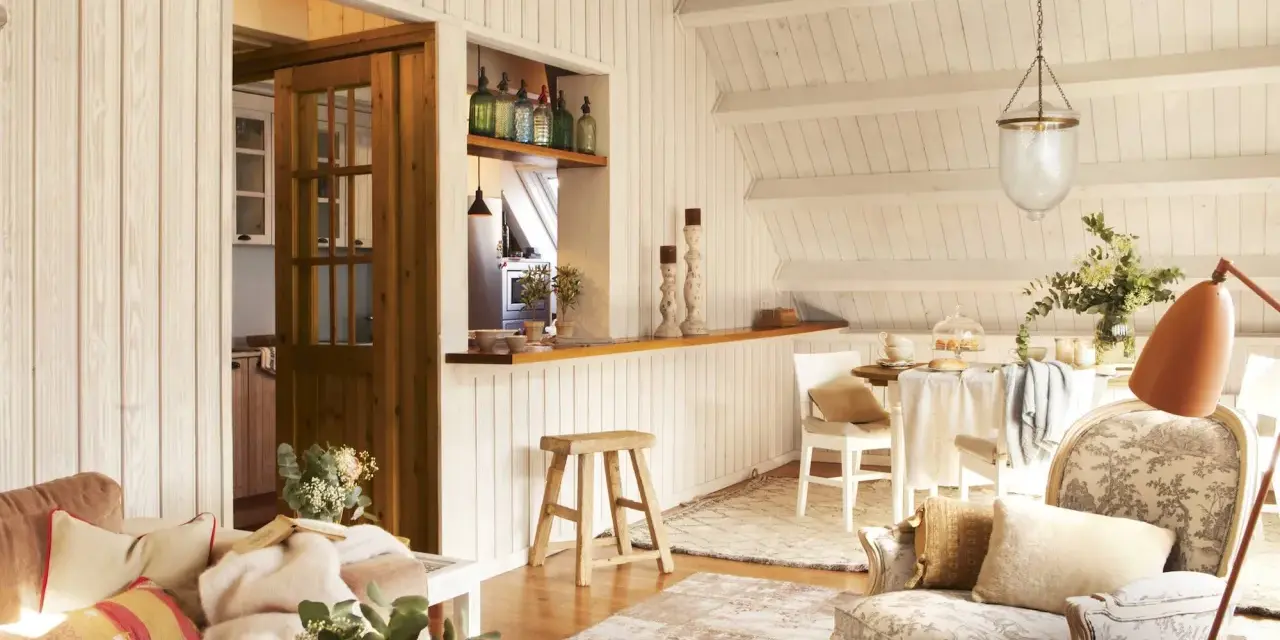 Acogedora buhardilla con encanto, con sofá, sillón estampado, mesa de comedor y cocina abierta.