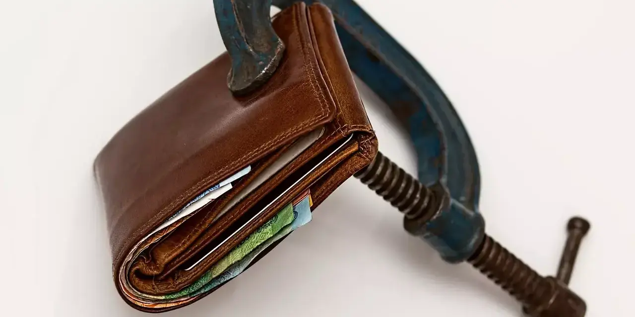 Cartera de cuero apretada en una prensa. El heredero no paga gastos de vivienda, el dinero está bajo presión.