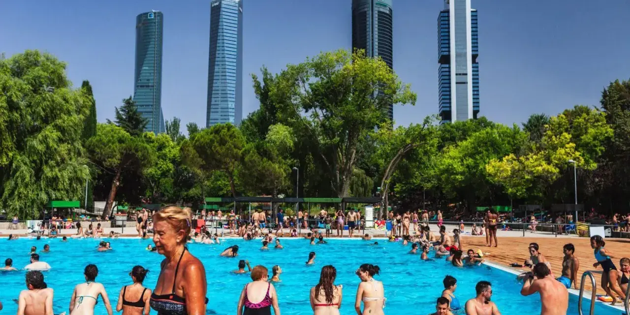 Gente disfrutando en una vibrante piscina comunitaria, con rascacielos modernos de fondo y árboles frondosos.