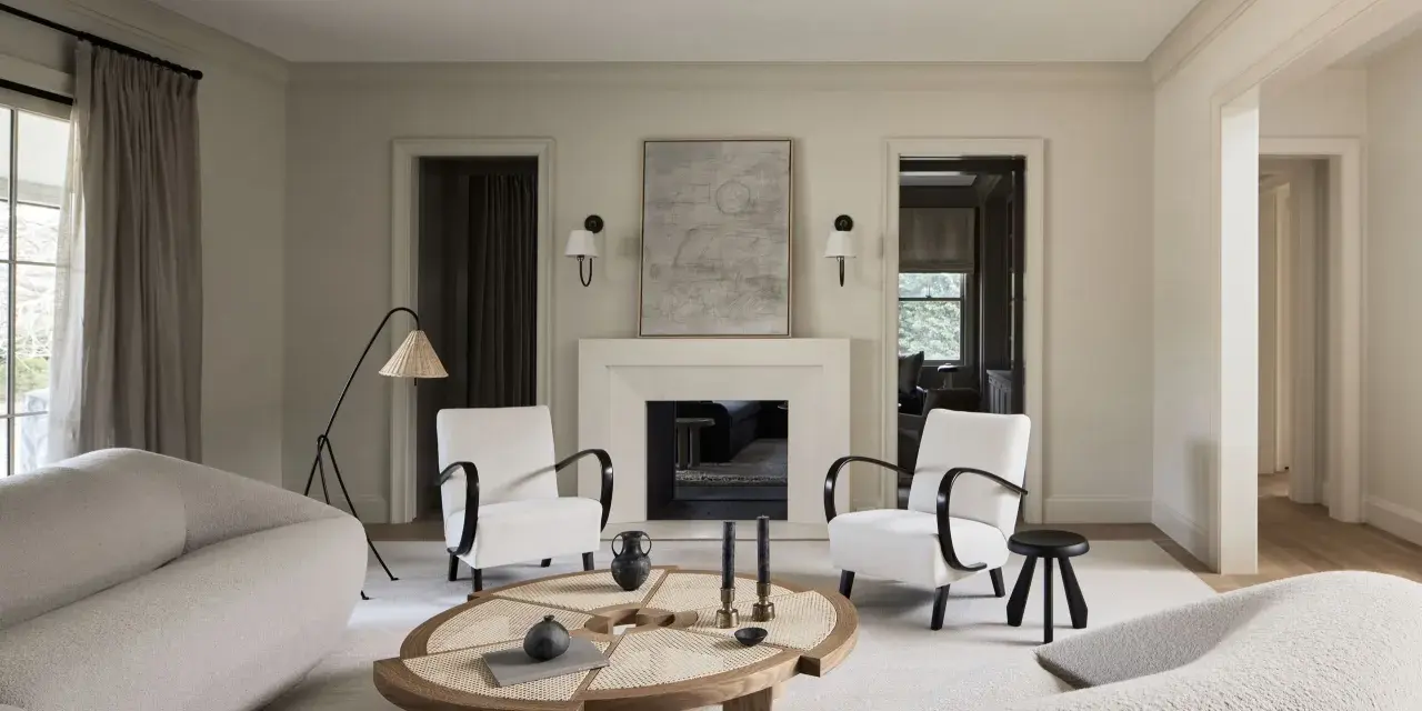 Sofá blanco texturizado, sillones blancos con brazos oscuros, mesa de centro de madera y ratán, chimenea y arte abstracto. Colores que combinan con el blanco crean un ambiente sereno.