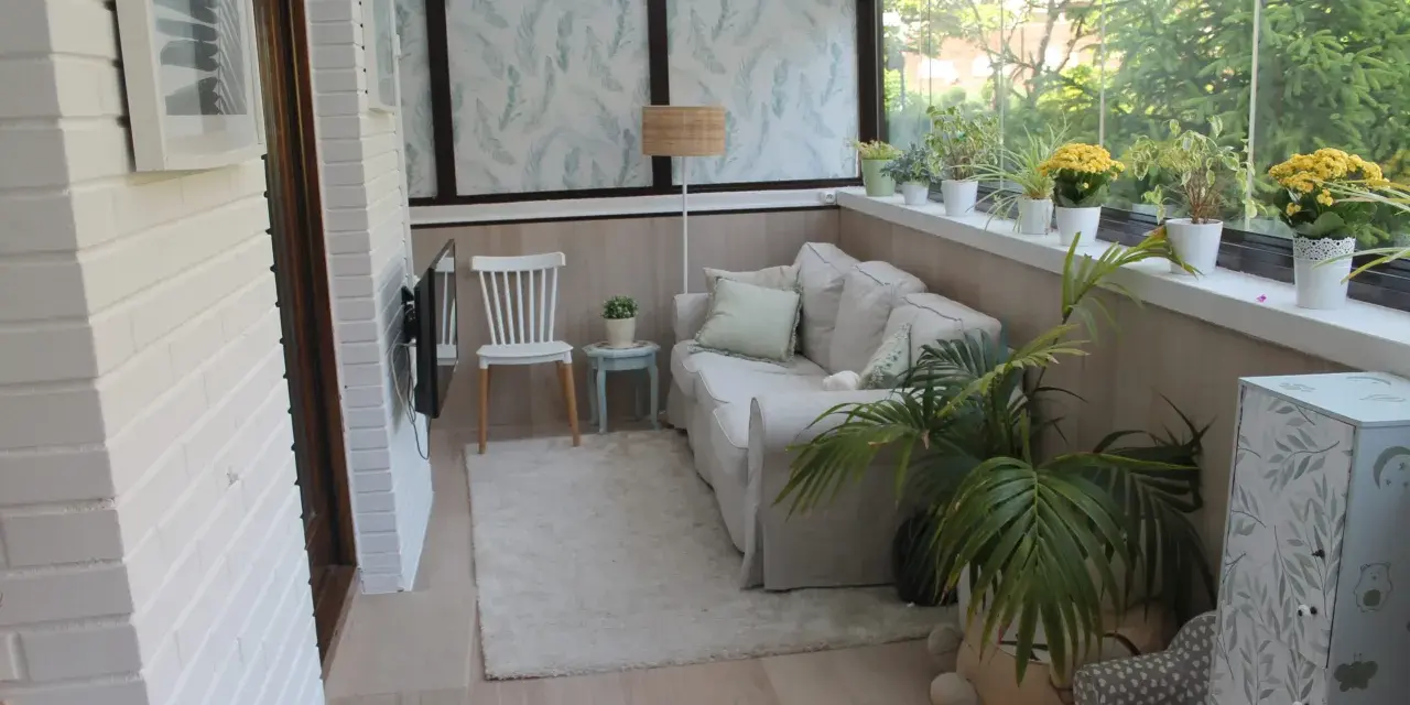 Acogedor salón en terrazas cerradas con encanto, con sofá, silla, plantas y vistas al exterior.
